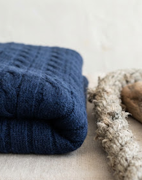 Folded navy cable-knit sweater beside rope